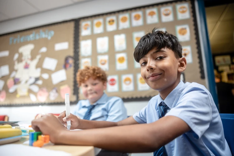 Two boys sitting at a school desk smiling with emojis behind them
