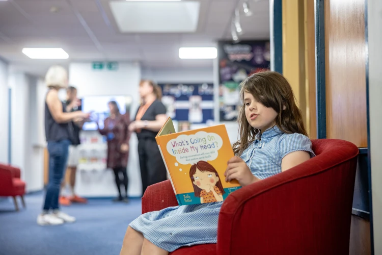 Young girl in school on a chair reading a book called 'What's Going On Inside My Head"