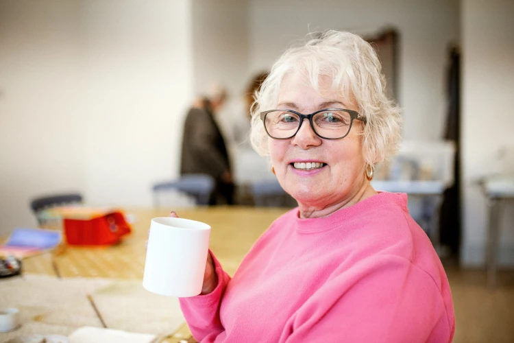 Woman in glasses and a pink jumper holding a cup of tea and smiling