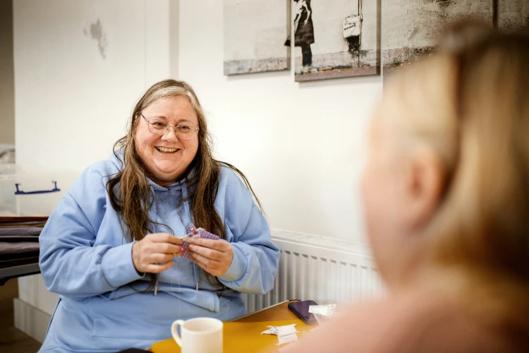 Woman in blue top wearing glasses looking towards another person and laughing