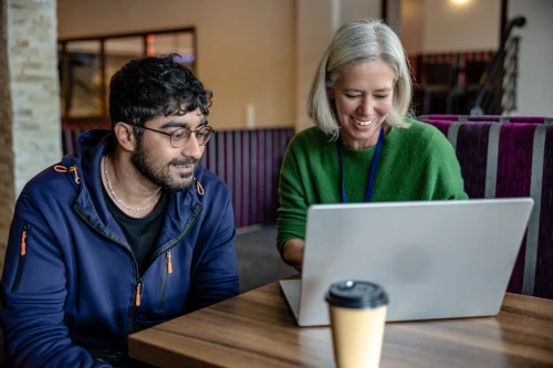 Man and woman sitting at lap top in cafe smiling