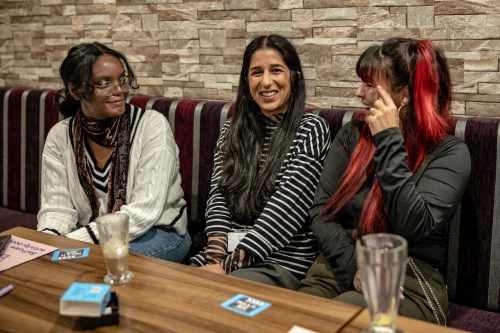 Three women sitting at a table laughing and drinking coffee