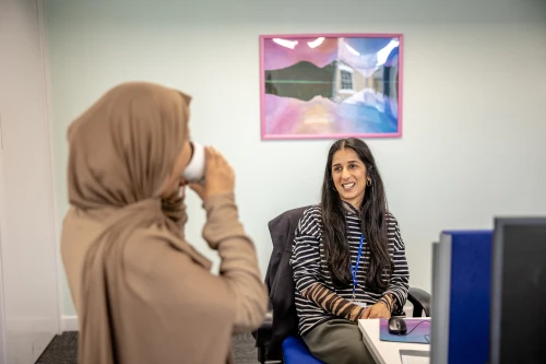 Woman sitting at desk talking to another woman
